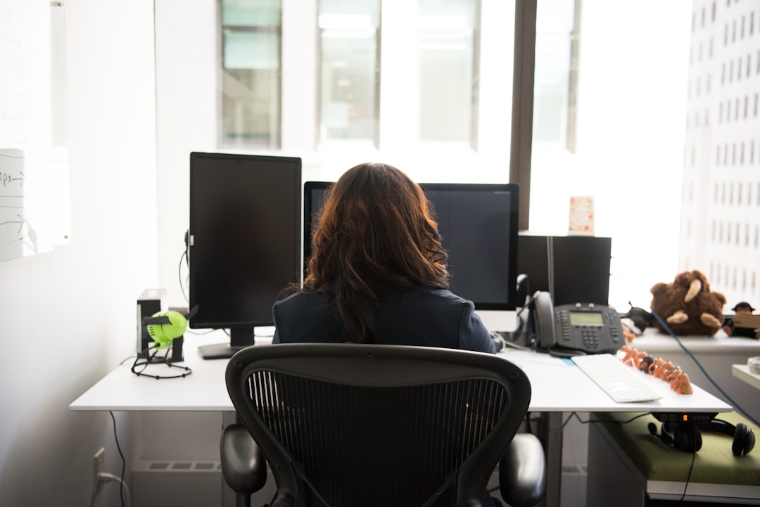 woman sitting on chair front of desk with desktop in office