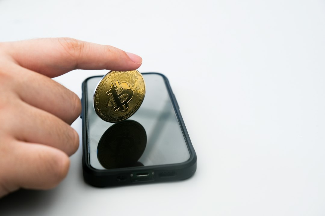 スマートフォンの前で金色のコインを持つ手