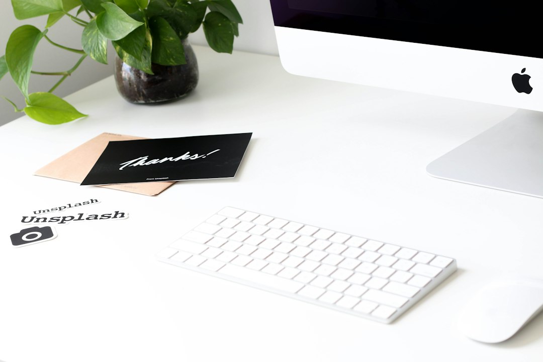 A Mac computer, keyboard and mouse on a desk with a plant